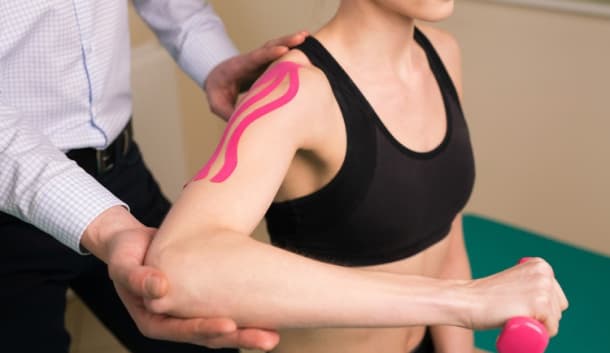 Terapeuta sosteniendo el brazo de una paciente con vendaje neuromuscular en el hombro